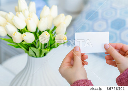 Woman pulling blank greeting card from bouquet of white tulips flowers. Mother day, Copy space. Mock up 86758501
