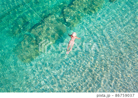 Top, aerial view. Young beautiful woman in a hat and white bikini swimming in sea water on the sand beach. Drone, copter photo. Summer vacation. View from above. Top, aerial view. Young beautiful woman in a hat and white bikini swimming in sea water on the sand beach. Drone, copter photo. Summer vacation. View from above. 86759037