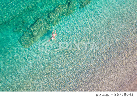 Top, aerial view. Young beautiful woman in a hat and white bikini swimming in sea water on the sand beach. Drone, copter photo. Summer vacation. View from above. Top, aerial view. Young beautiful woman in a hat and white bikini swimming in sea water on the sand beach. Drone, copter photo. Summer vacation. View from above. 86759043