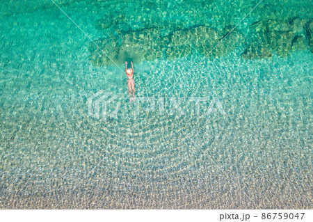 Top, aerial view. Young beautiful woman in a hat and white bikini swimming in sea water on the sand beach. Drone, copter photo. Summer vacation. View from above. Top, aerial view. Young beautiful woman in a hat and white bikini swimming in sea water on the sand beach. Drone, copter photo. Summer vacation. View from above. 86759047