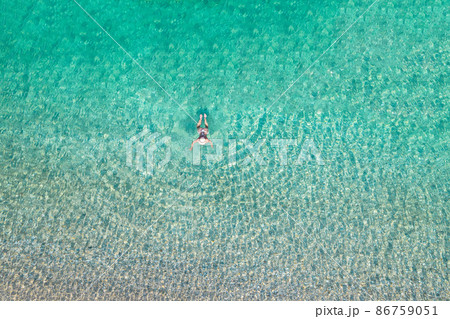 Top, aerial view. Young beautiful woman in a hat and white bikini swimming in sea water on the sand beach. Drone, copter photo. Summer vacation. View from above. Top, aerial view. Young beautiful woman in a hat and white bikini swimming in sea water on the sand beach. Drone, copter photo. Summer vacation. View from above. 86759051