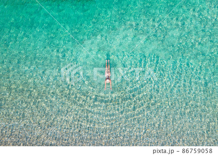 Top, aerial view. Young beautiful woman in a hat and white bikini swimming in sea water on the sand beach. Drone, copter photo. Summer vacation. View from above. Top, aerial view. Young beautiful woman in a hat and white bikini swimming in sea water on the sand beach. Drone, copter photo. Summer vacation. View from above. 86759058