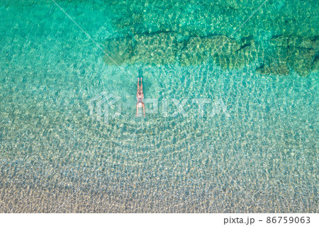 Top, aerial view. Young beautiful woman in a hat and white bikini swimming in sea water on the sand beach. Drone, copter photo. Summer vacation. View from above. Top, aerial view. Young beautiful woman in a hat and white bikini swimming in sea water on the sand beach. Drone, copter photo. Summer vacation. View from above. 86759063