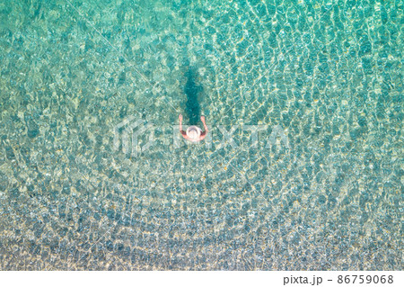 Top, aerial view. Young beautiful woman in a hat and white bikini swimming in sea water on the sand beach. Drone, copter photo. Summer vacation. View from above. Top, aerial view. Young beautiful woman in a hat and white bikini swimming in sea water on the sand beach. Drone, copter photo. Summer vacation. View from above. 86759068