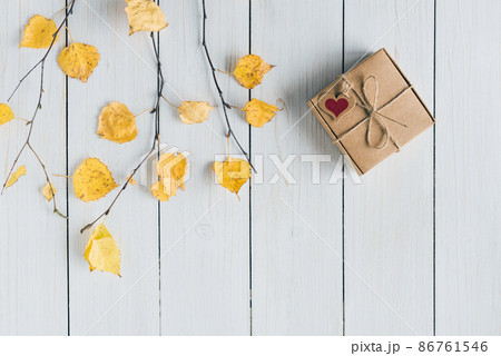 Woman packing gift in a box of kraft paper on white retro wood boards. leaves, birch branches. Thanksgiving. Autumn, fall concept. Flat lay, top view. 86761546