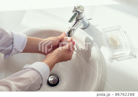 Woman washing hands rubbing with soap in white sink in bathroom with sunlight from the window. Protection from bacteria and virus. Hygienic concept. Top view Woman washing hands rubbing with soap in white sink in bathroom with sunlight from the window. Protection from bacteria and virus. Hygienic concept. Top view 86762288