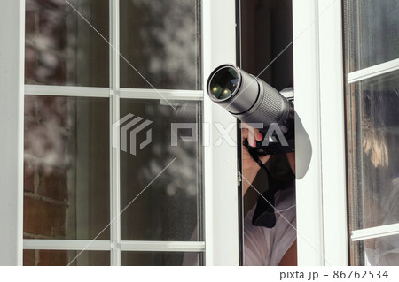 Private detective with spying zoom lens camera taking picture through open window. Closeup. concept Private detective with spying zoom lens camera taking picture through open window. Closeup. concept 86762534