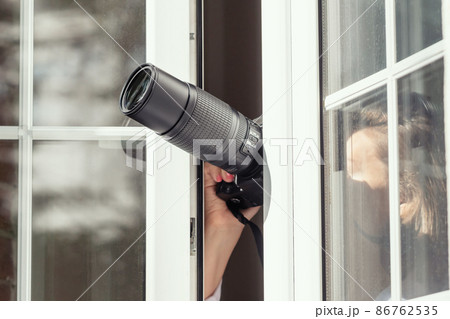 Private detective with spying zoom lens camera taking picture through open window. Closeup. concept Private detective with spying zoom lens camera taking picture through open window. Closeup. concept 86762535