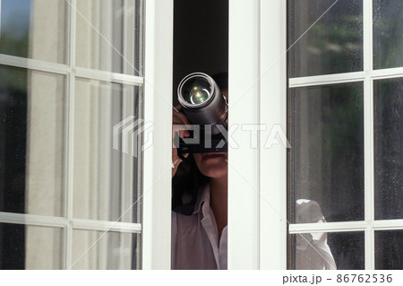 Private detective with spying zoom lens camera taking picture through open window. Closeup. concept Private detective with spying zoom lens camera taking picture through open window. Closeup. concept 86762536