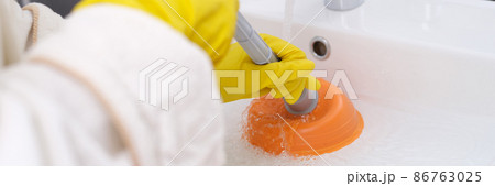 Person in yellow gloves is cleaning sink from blockage closeup Person in yellow gloves is cleaning sink from blockage closeup 86763025