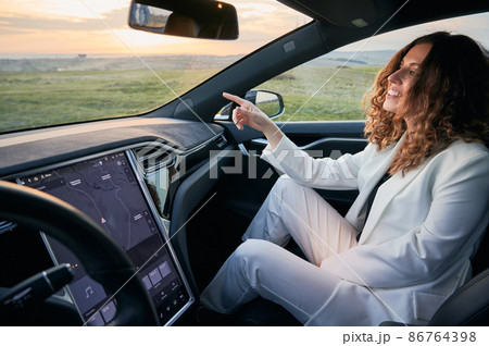 POV young business woman sitting in passenger seat next to driver and pointing finger in front of her. Background of fields and sunset. 86764398