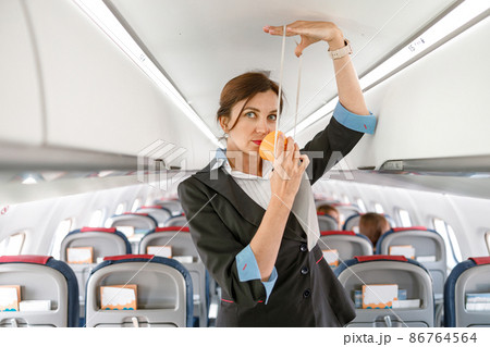 Female stewardess demonstrating how to use oxygen mask in plane Female stewardess demonstrating how to use oxygen mask in plane 86764564