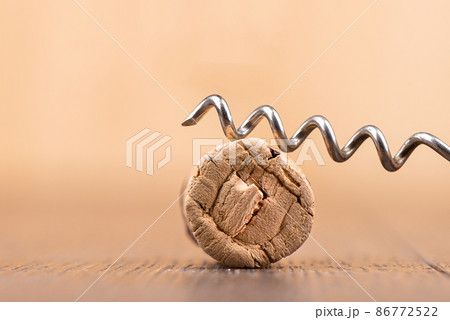 Close-up of a corkscrew on top of a wine cork on a wooden surface. Close-up of a corkscrew on top of a wine cork on a wooden surface. 86772522