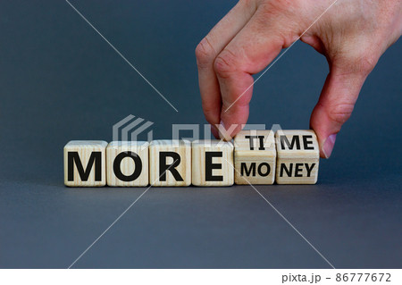 More time or more money. Male hand flips wooden cubes and changes the inscription 'more money' to 'more time' or vice versa. Beautiful grey background, copy space. Concept. 86777672