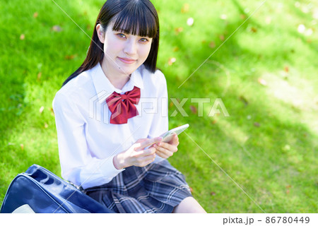 綺麗な新緑の公園の芝生でスマホを使う女子高校生　アプリ　SNS　携帯電話　見下ろし構図　俯瞰 86780449