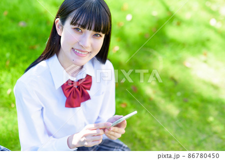 綺麗な新緑の公園の芝生でスマホを使う女子高校生　アプリ　SNS　携帯電話　見下ろし構図　俯瞰 86780450