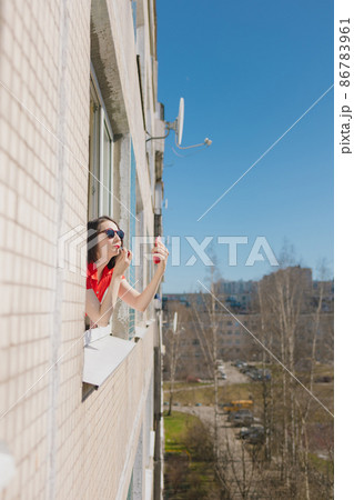 a pretty woman in a red dress looks out the window of her house 86783961
