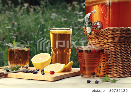 Homemade mushroom kombucha drink in a jar with a tap and in glasses with mint, berries and lemon on a wooden table Homemade mushroom kombucha drink in a jar with a tap and in glasses with mint, berries and lemon on a wooden table 86785126