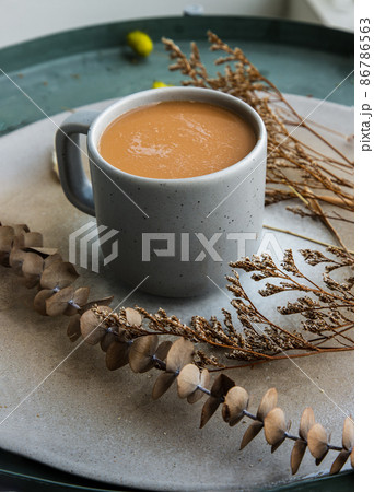 Hot orange milk tea in a blue ceramic cup, Sweet refreshment thai milk tea on ceramic and dried flowers on ceramic plate. Hot orange milk tea in a blue ceramic cup, Sweet refreshment thai milk tea on ceramic and dried flowers on ceramic plate. 86786563