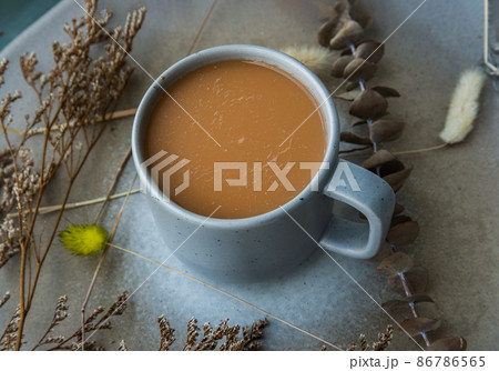 Hot orange milk tea in a blue ceramic cup, Sweet refreshment thai milk tea on ceramic and dried flowers on ceramic plate. Hot orange milk tea in a blue ceramic cup, Sweet refreshment thai milk tea on ceramic and dried flowers on ceramic plate. 86786565