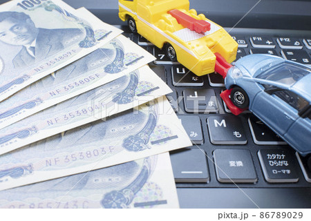 千円札とパソコンのキーボードとレッカー車に引かれているコンパクトカー 86789029