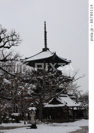 灰色の冬空から雪が降り三重塔や手洗い場の屋根や石灯籠や木々等に積雪のある寺の境内の冬の雪化粧した風景 86789114