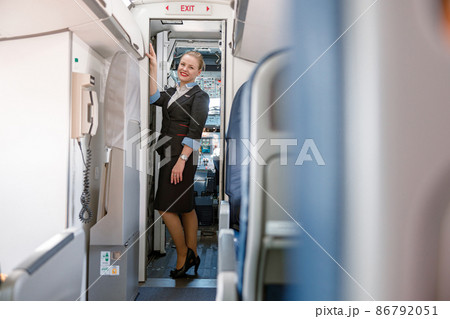 Cheerful stewardess standing at exit door in airplane 86792051