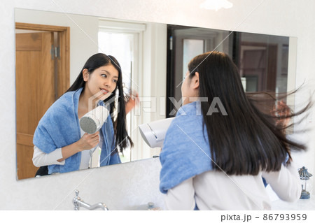 鏡の前でドライヤーで髪を乾かしている若い女性 86793959