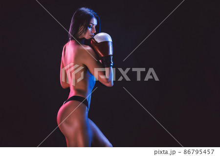 erotic studio shot of young brunette athlete woman in boxing gloves who stands on black background 86795457