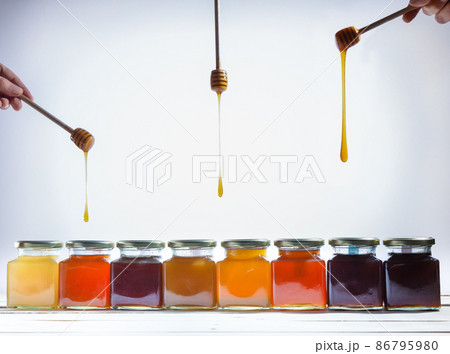 Jars of honey and sticks spilling honey on white background. 86795980