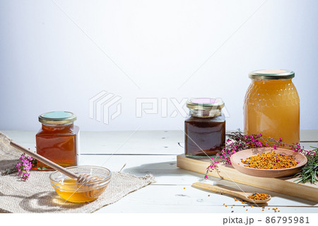 Honey  jars with honey sticks ,flowers and bee pollen on wooden white background 86795981