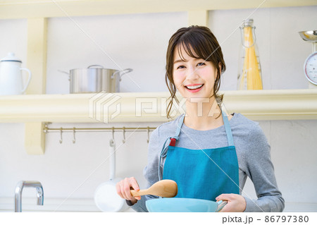 キッチンで炒め物をするエプロン姿の若い主婦 キッチンで炒め物をするエプロン姿の若い主婦 86797380