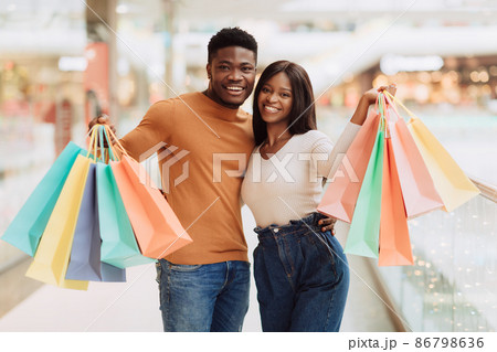 Beautiful black couple holding shopping bags looking at camera Beautiful black couple holding shopping bags looking at camera 86798636