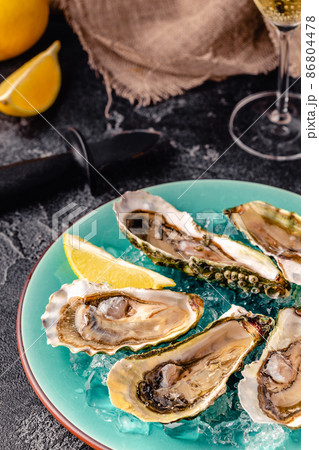 Opened fresh oysters on a blue plate, served with lemon and ice. 86804478