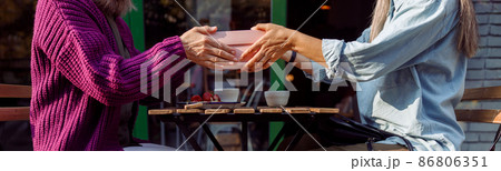 Senior women friends hold gift box above table on outdoors cafe terrace Senior women friends hold gift box above table on outdoors cafe terrace 86806351