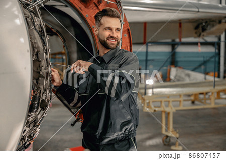 Cheerful male mechanic repairing aircraft in hangar 86807457