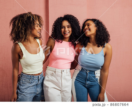 Three cheerful women with curly hair having fun together while standing at a pink wall Three cheerful women with curly hair having fun together while standing at a pink wall 86807664