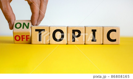 Hand turns a cube and changes the expression 'off topic' to 'on topic'. Beautiful yellow table, white background. Business concept. Copy space. Hand turns a cube and changes the expression 'off topic' to 'on topic'. Beautiful yellow table, white background. Business concept. Copy space. 86808165