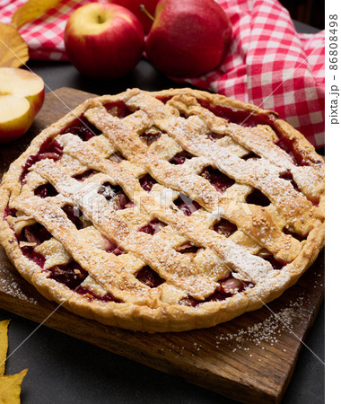baked round traditional apple pie on brown wooden board and fresh red apples, top view 86808498