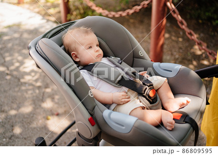 a little boy lies strapped in a stroller-carrier.  86809595