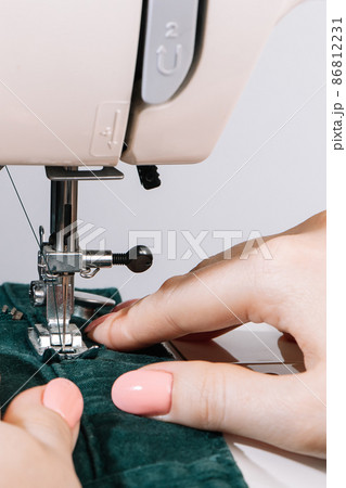 Woman tailor works on sewing machine. Hands hold fabric. World tailors day. Close-up of sewing process. Home clothing repair. Woman tailor works on sewing machine. Hands hold fabric. World tailors day. Close-up of sewing process. Home clothing repair. 86812231