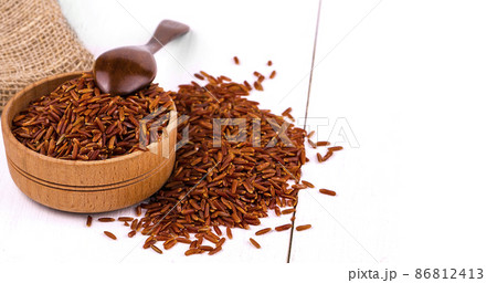 Dark rice, burlap and spoon in a wooden cup on a white dining table. Dark rice, burlap and spoon in a wooden cup on a white dining table. 86812413