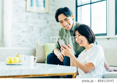 リビングでスマホを見る若い夫婦 リビングでスマホを見る若い夫婦 86813045