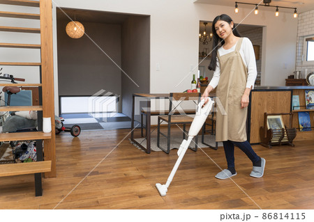 ハンディー掃除機でリビングの掃除をする若い女性 86814115