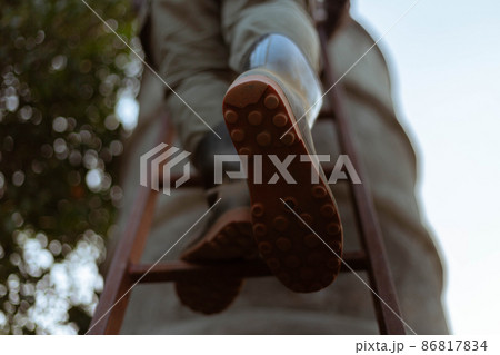 Gardening concept a male farmer wearing big boots climbing on a wooden ladder to a cement water tank 86817834