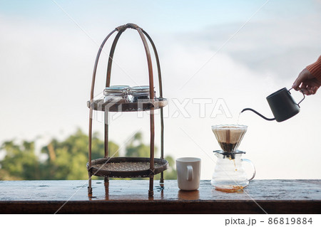 Hand pouring Hot water during brewing arabica coffee by Vintage coffee drip equipment on wooden table in the morning with mountain and nature background Hand pouring Hot water during brewing arabica coffee by Vintage coffee drip equipment on wooden table in the morning with mountain and nature background 86819884