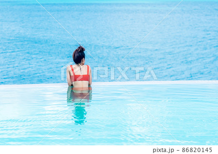 Happy woman in orange swimsuit swimming in infinity pool at luxury hotel against ocean front. young female enjoy in tropical resort. Relaxing, summer,  travel, holiday, vacation and weekend concept 86820145