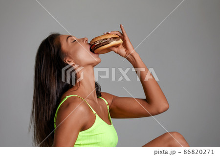 Sexy athletic woman eating hamburger on gray background 86820271