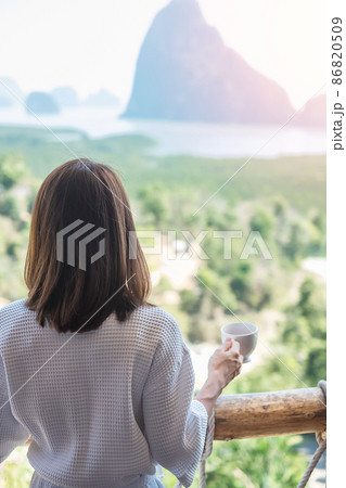 happy woman in bathrobe holding hot coffee cup or tea mug after waking up and enjoy Phang Nga bay view point, Tourist relaxing in tropical resort at Samet Nang She. Travel summer vacation concept happy woman in bathrobe holding hot coffee cup or tea mug after waking up and enjoy Phang Nga bay view point, Tourist relaxing in tropical resort at Samet Nang She. Travel summer vacation concept 86820509