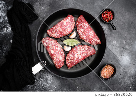 Ground raw meat patties. Meat cutlet ready to cook. Farm organic meat, in cast iron frying pan, on black dark stone table background, top view flat lay Ground raw meat patties. Meat cutlet ready to cook. Farm organic meat, in cast iron frying pan, on black dark stone table background, top view flat lay 86820620